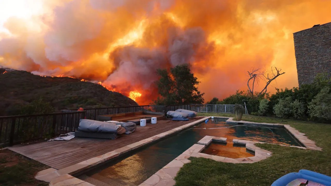 Wildfire smoke and flames behind a home's backyard pool and patio
